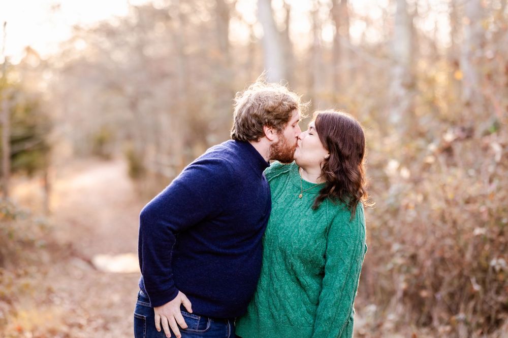 A couple shares an intimate moment on a leaf-covered forest path in autumn.