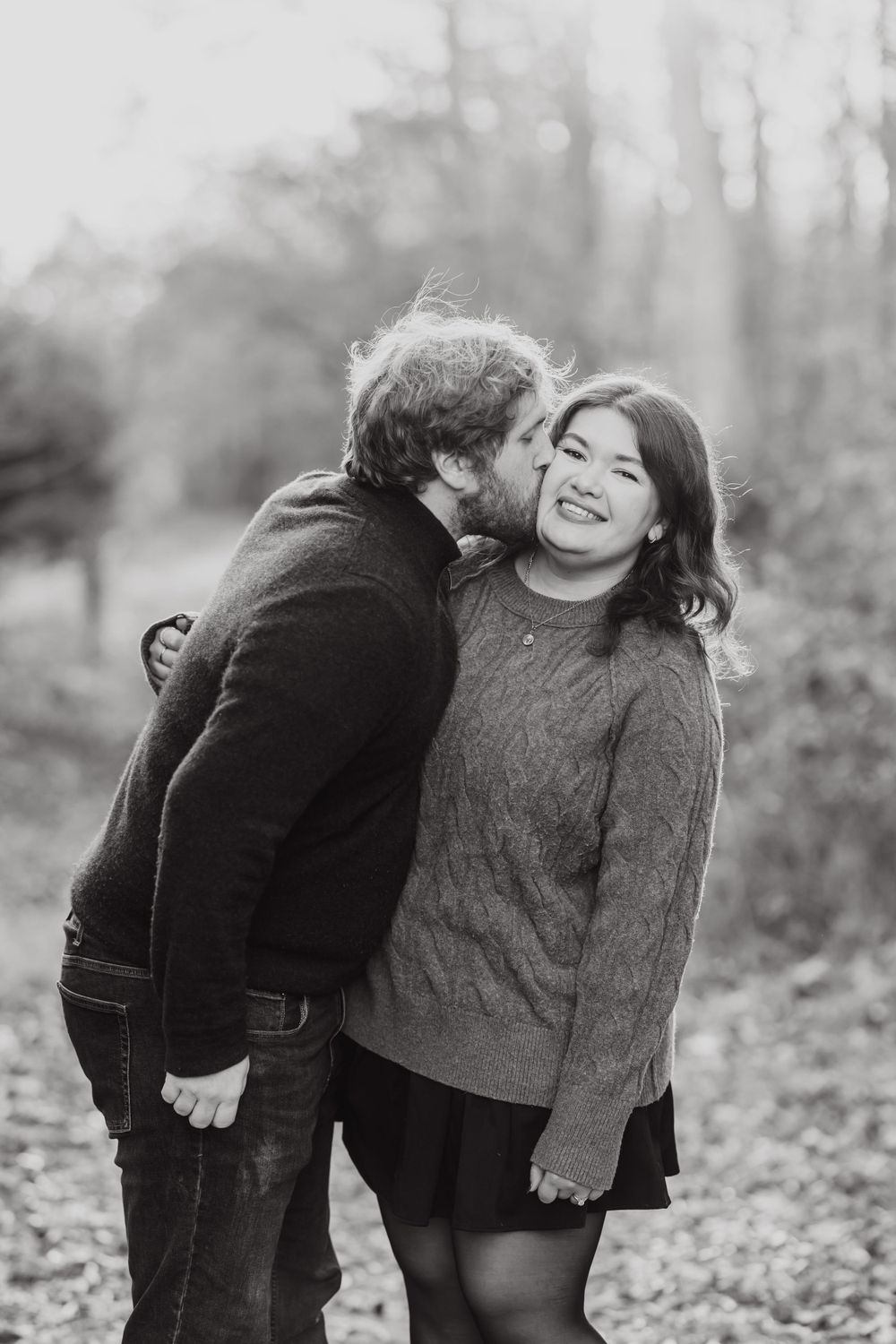 A candid black and white photo capturing a joyful intimate moment between two people on a forest path.