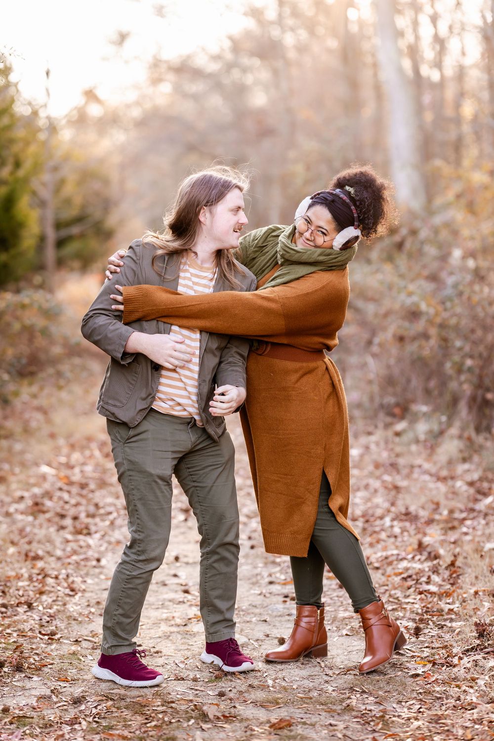 A playful couple embraces while laughing on a leaf-covered trail in fall.