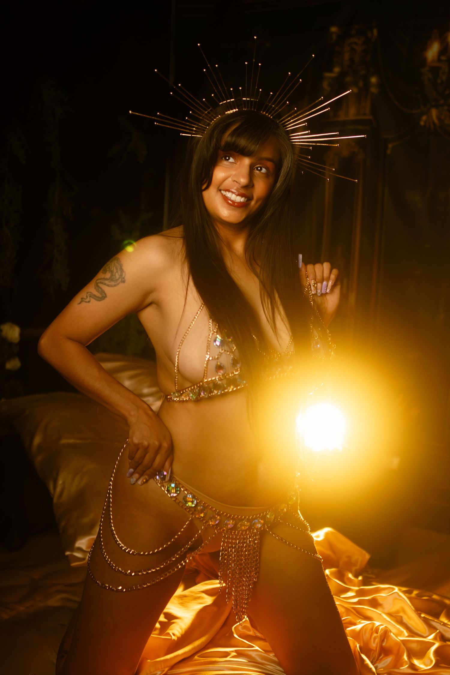 A figure in a glittering outfit with a spiked halo headpiece poses dramatically against a golden-lit dark backdrop for her empowerment shoot