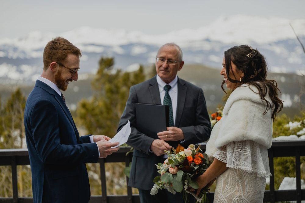 A couple exchanges vows during an intimate mountain wedding ceremony on a scenic outdoor deck with fall foliage.