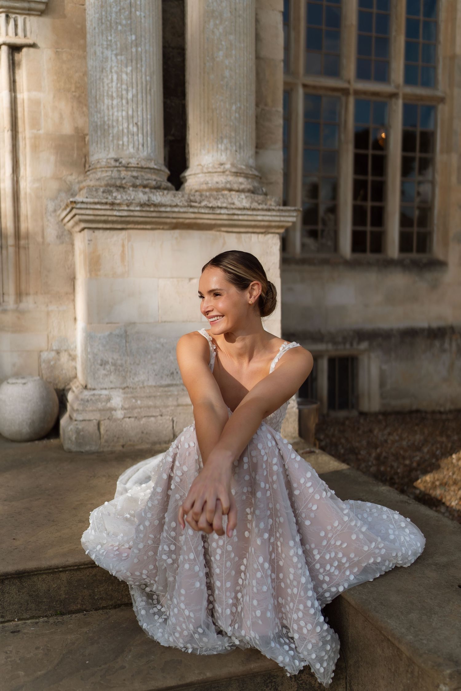 A sparkly white polka dot dress catches the evening light as someone sits gracefully on stone steps by classic columns.
