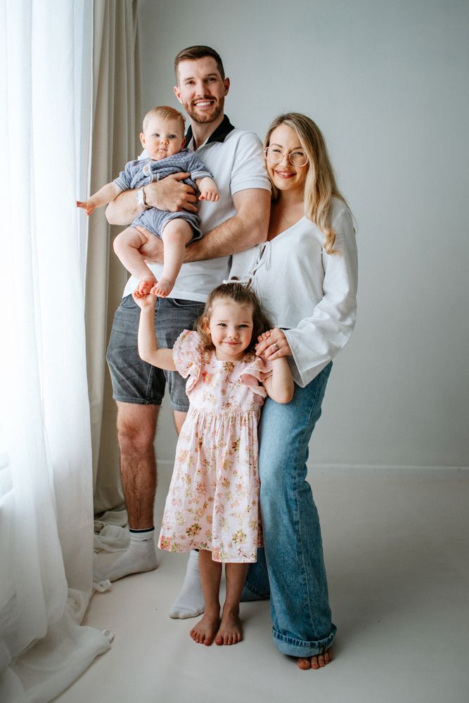 A family in white clothing sharing a joyful moment together against a light background.
