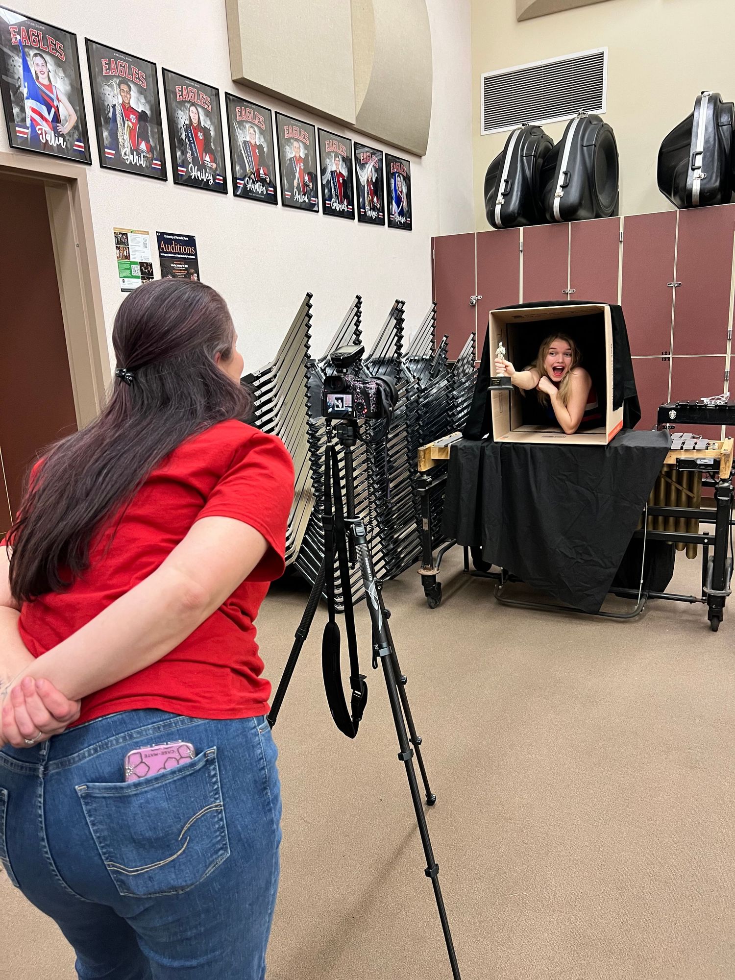 A photography session setup in a studio with a tripod and lighting equipment facing a prop box display against a wall.