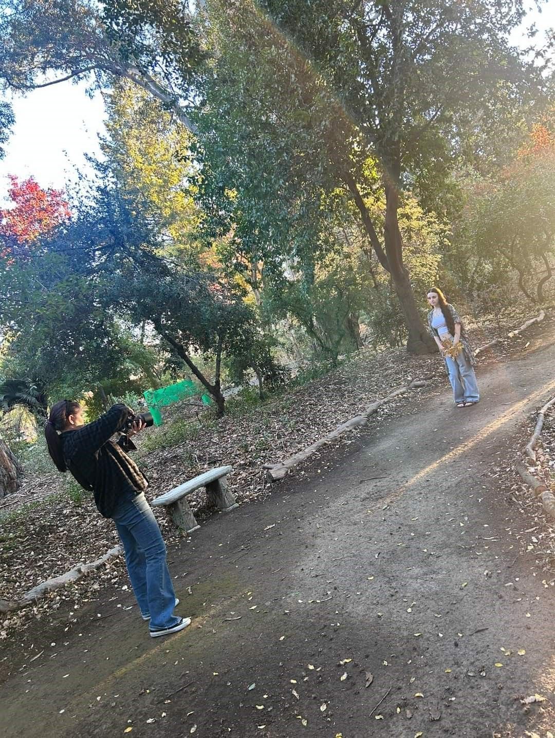 Photographer on a sloping dirt path surrounded by autumn trees and fallen leaves.