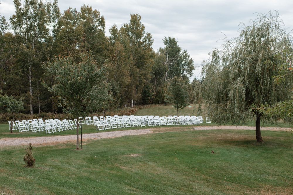 Rows of white chairs set up for an outdoor wedding ceremony on a green lawn surrounded by trees.