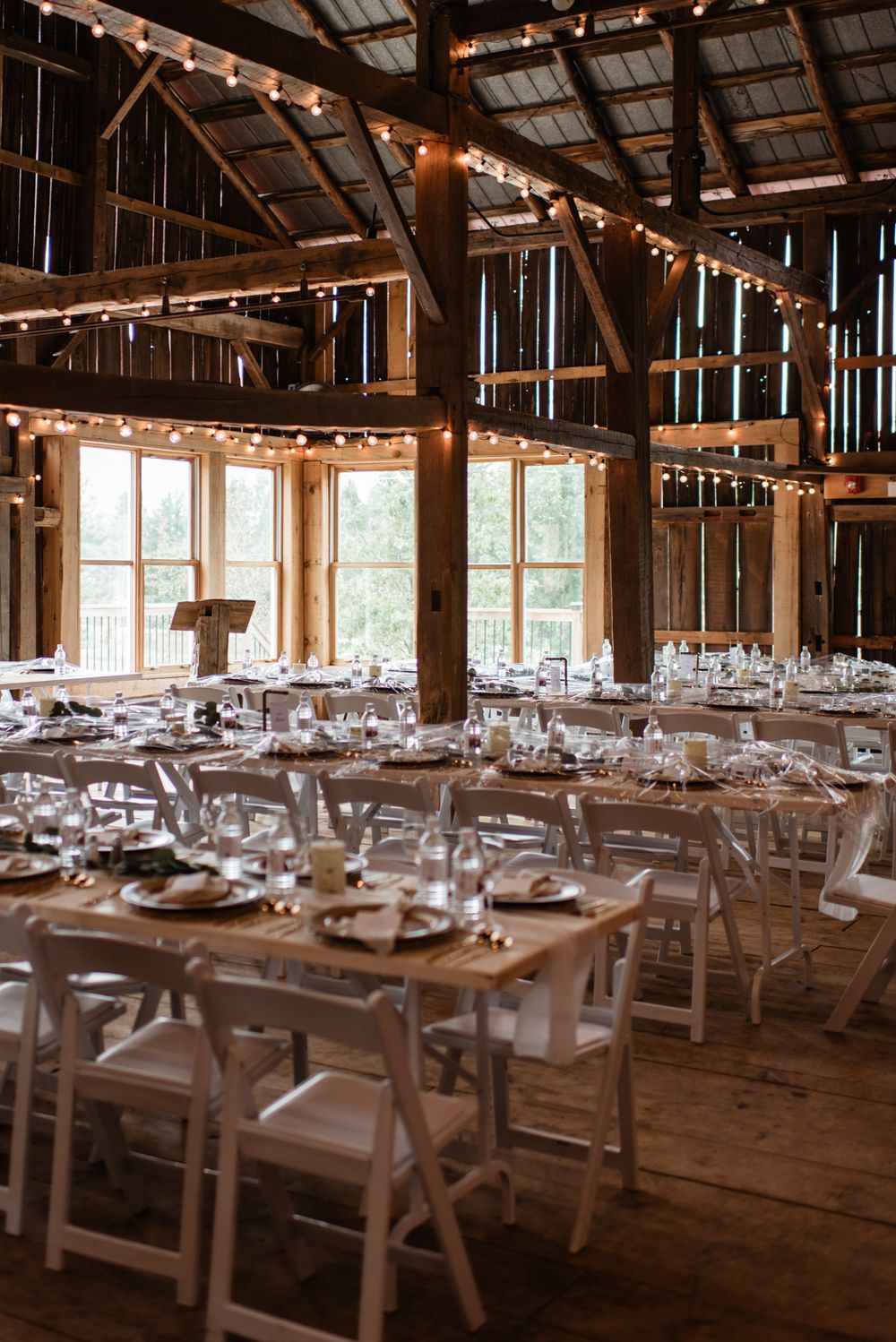 Rustic barn wedding reception venue with wooden tables, white folding chairs and string lights decorating the rafters.