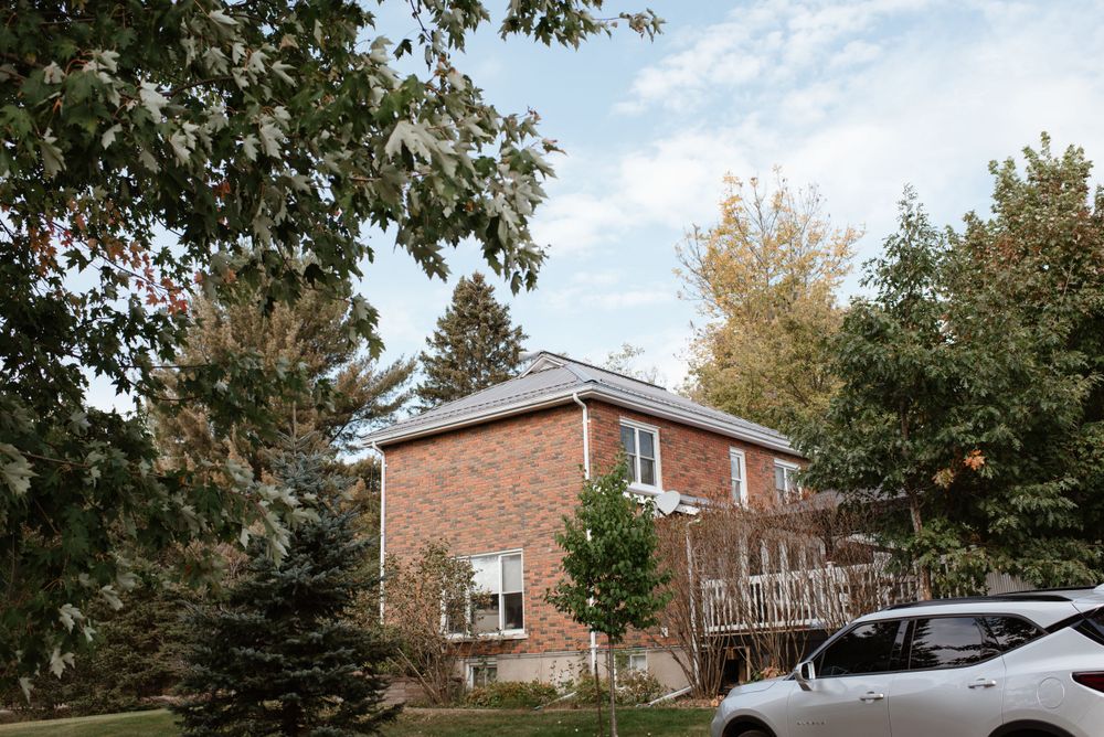 A red brick house surrounded by autumn trees with a parked car in the driveway.