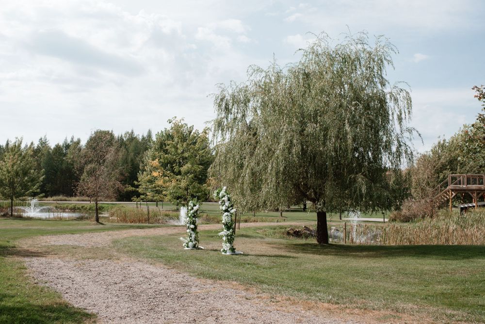 A gravel path leads through a serene garden with a weeping willow tree and decorative archway in the background.