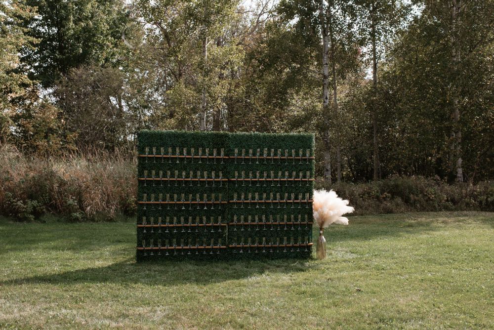 A decorative wall of green wine bottles arranged in a grid pattern stands on a grassy lawn with trees in the background.