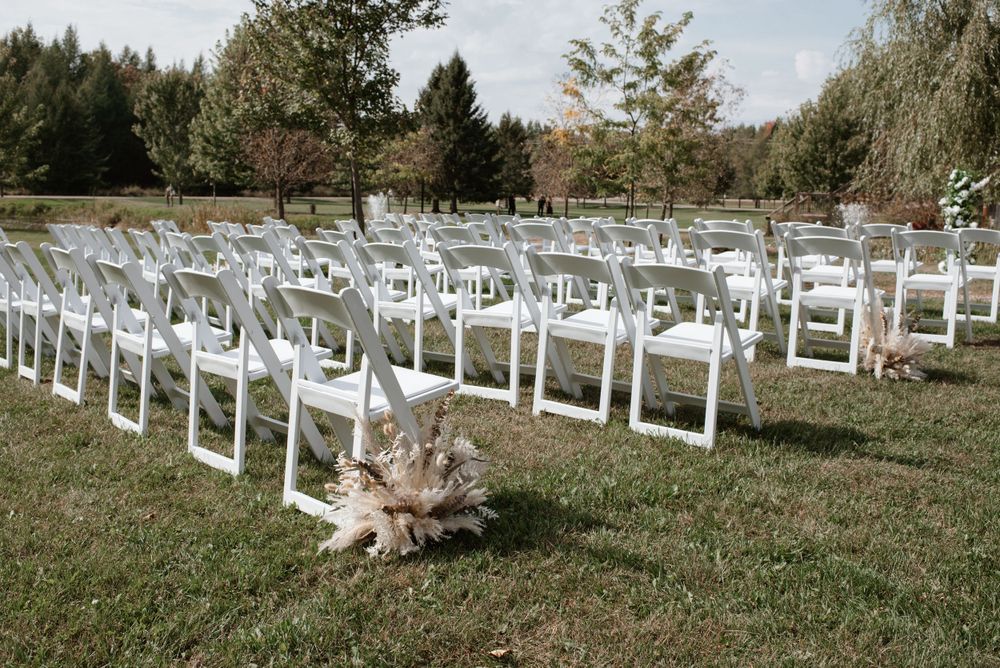 White folding chairs arranged for an outdoor wedding ceremony on a grassy lawn with trees in the background.