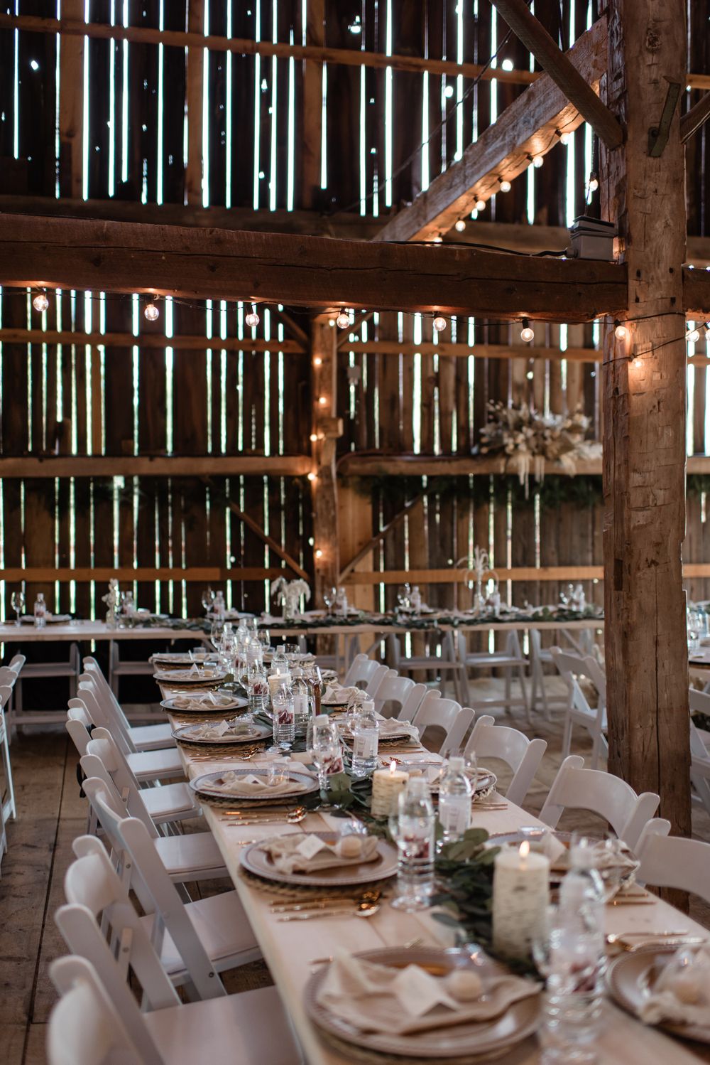 Rustic barn reception setup with long tables, string lights, and elegant place settings.