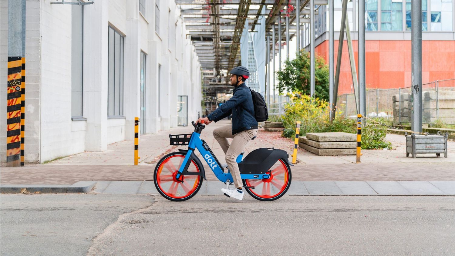 Urban cyclist riding a red and blue bikeshare bicycle along a city sidewalk.
