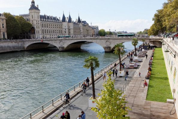 Seine riverbank promenade with cyclists and pedestrians near historic Parisian architecture.