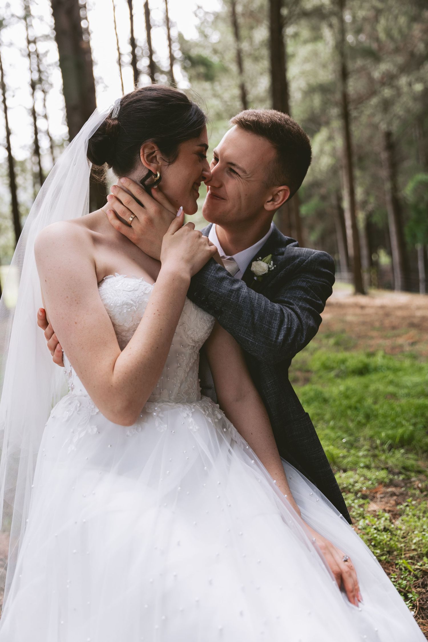 A romantic wedding moment captured in a forest setting with soft natural lighting.