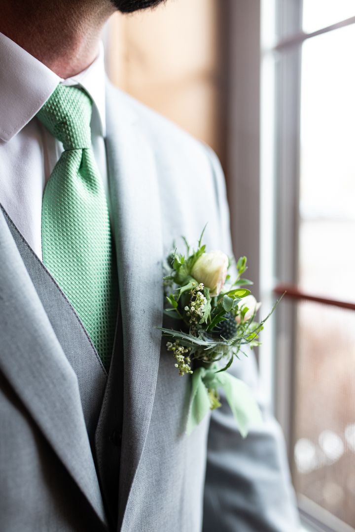 Detailed shot of mint green tie and floral boutonniere against light gray suit jacket.