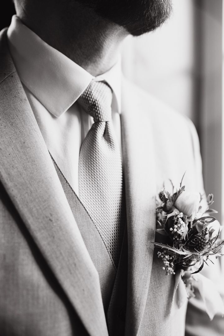 Close-up detail of boutonniere on light gray suit lapel with textured tie.