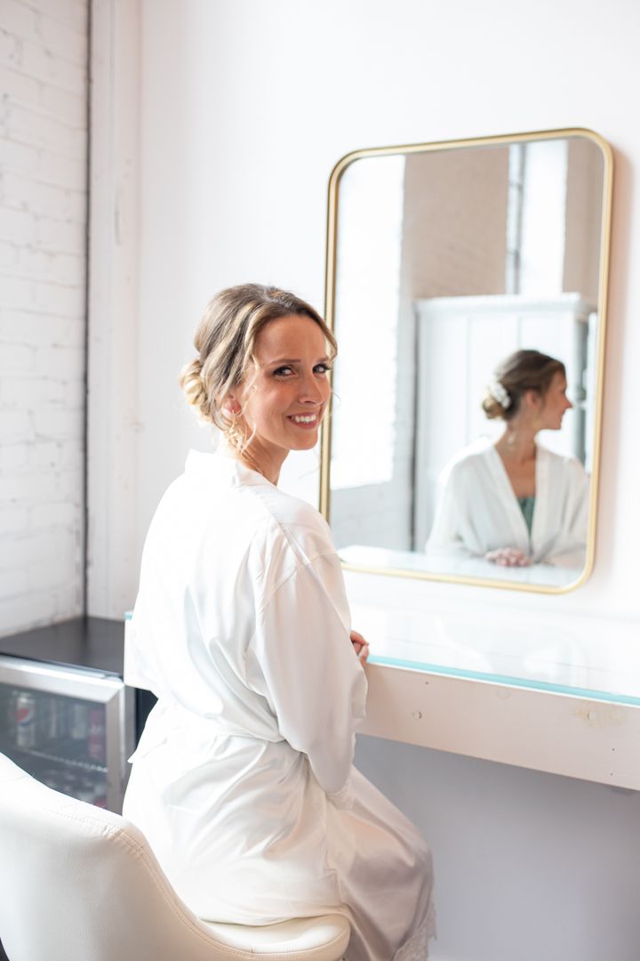 Getting ready scene with white robe and elegant updo reflected in gold-framed mirror.