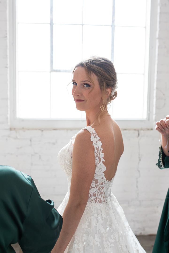 A side view of an elegant white lace wedding dress in a bright room with white brick walls.