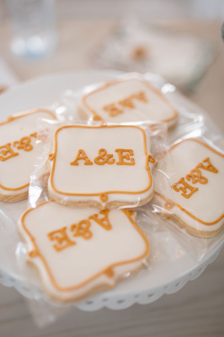 White frosted cookies with gold A&E monogram on delicate lace-edged plate.