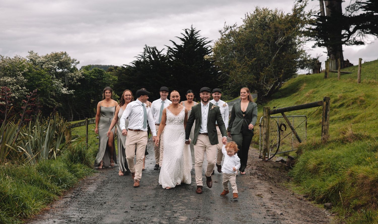 Wedding group walking down a hillside path surrounded by green landscape.