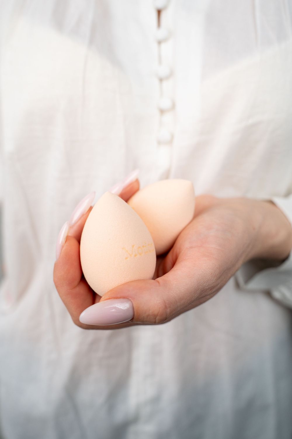 Beauty blending sponges held in hands wearing white flowing fabric.