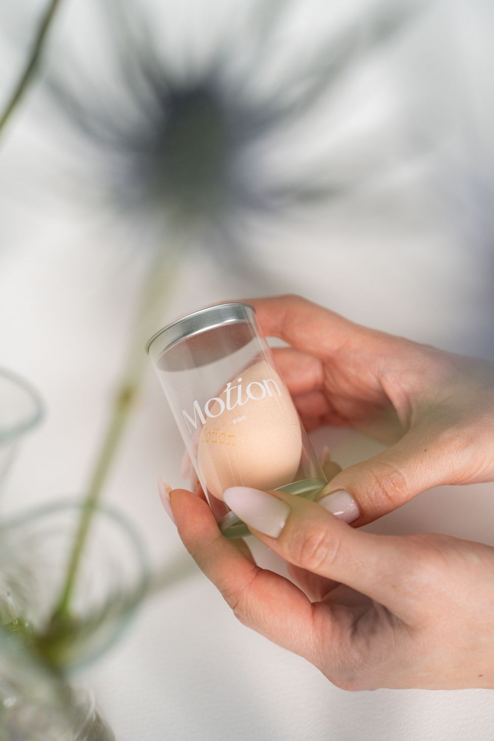 Close-up of hands holding a peach-colored makeup sponge in a clear cylindrical container with 'Motion' branding.