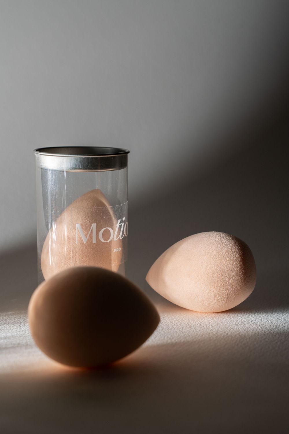 Three makeup blending sponges arranged with one in clear Motion-branded container.