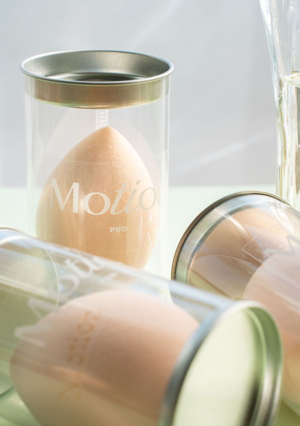 Motion makeup sponges in clear cylindrical containers shot with soft lighting and minimal styling.