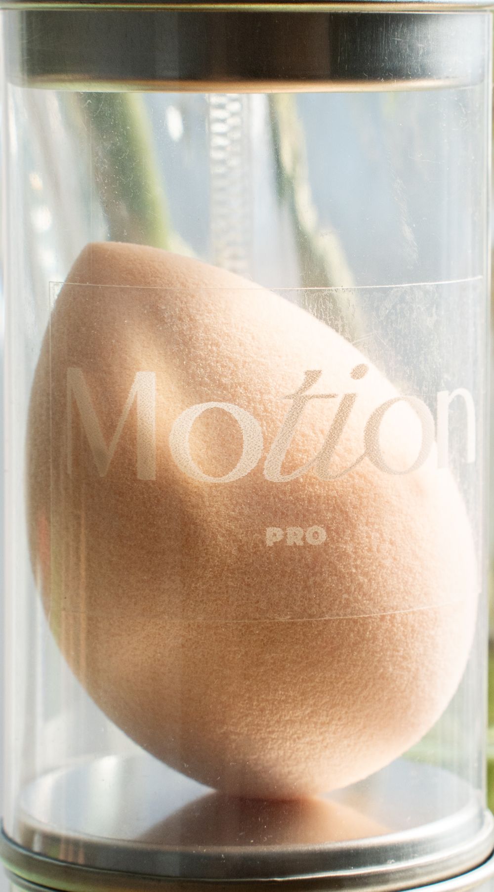 Close-up of peach-colored Motion Pro makeup sponge displayed in clear cylindrical container.