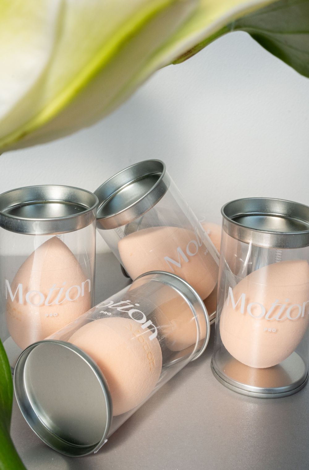 Scattered clear containers with Motion branding holding makeup sponges on white surface.