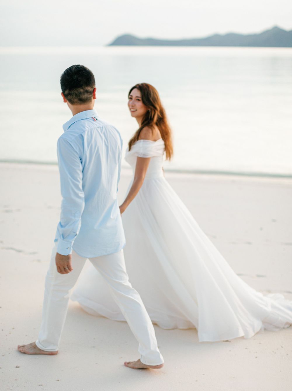 A newly married couple walking on the beach of Amanpulo, Philippines, hand in hand, with ocean in the backgroud.