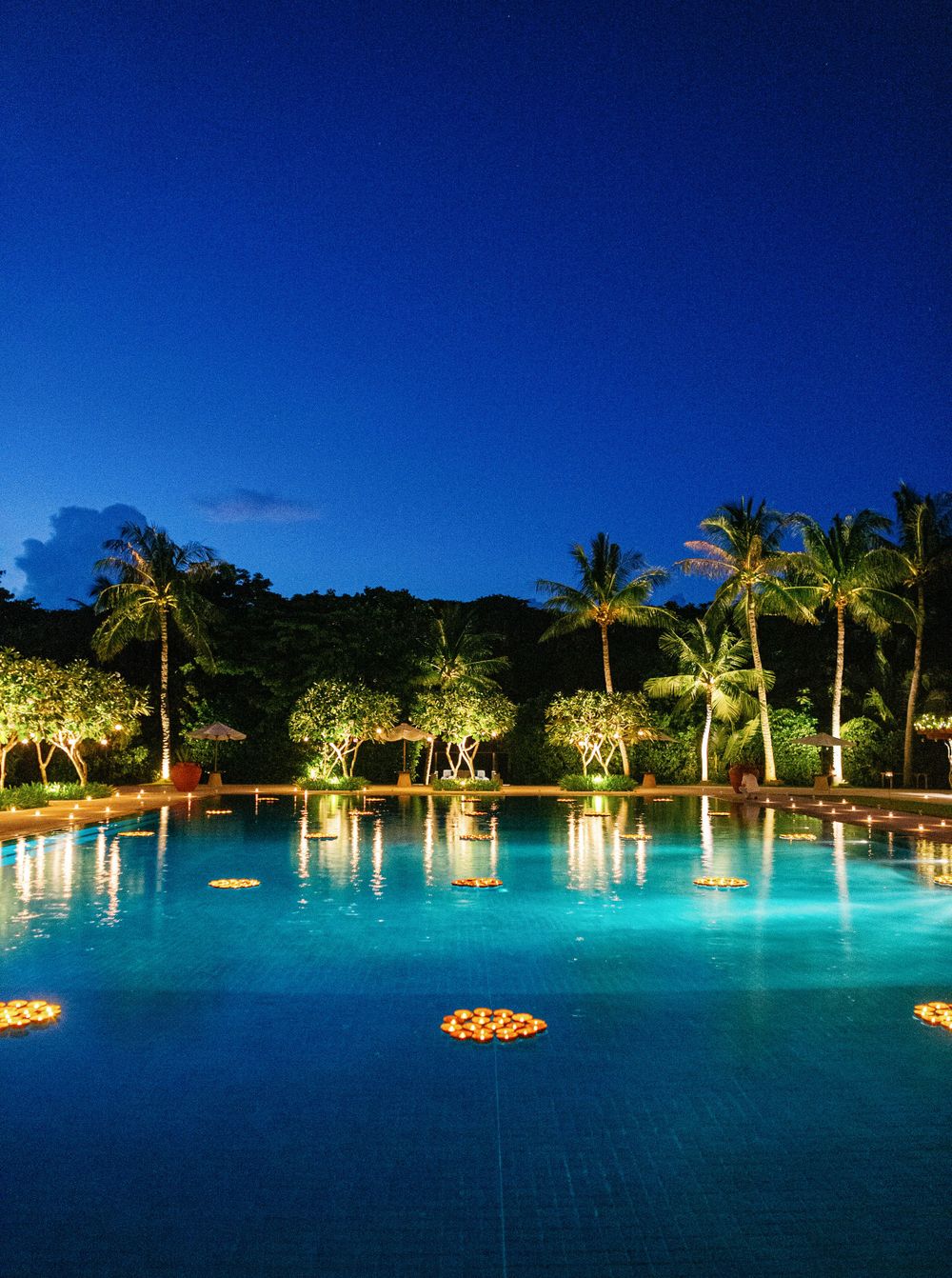 A serene swimming pool surrounded by Palms after sunset at Aman resort, Amanpulo, Philippines.