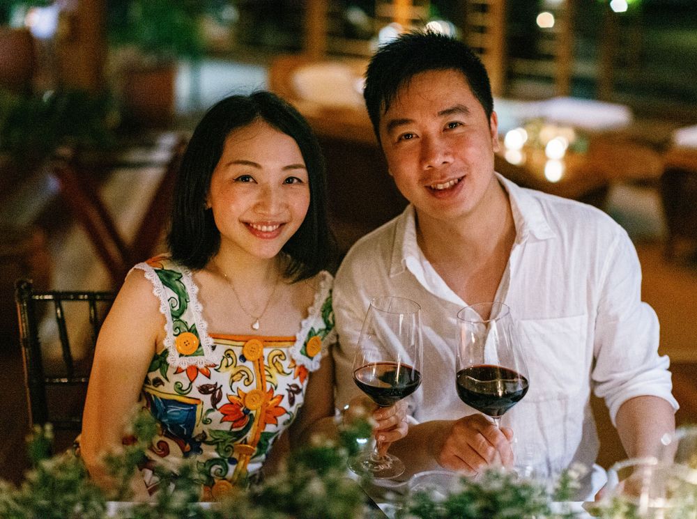 A happy couple holding wine glasses at a dinner table, smiling. Wedding reception at Aman resort in Amanpulo.