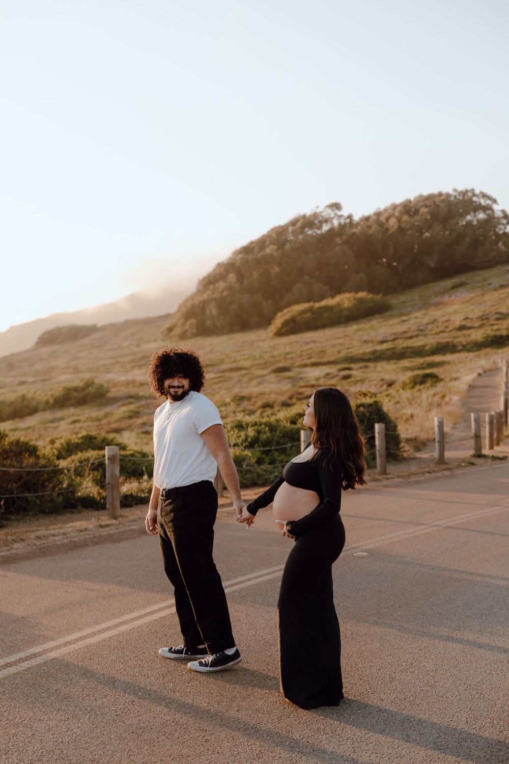 A couple shares a playful moment on a coastal path during golden hour.