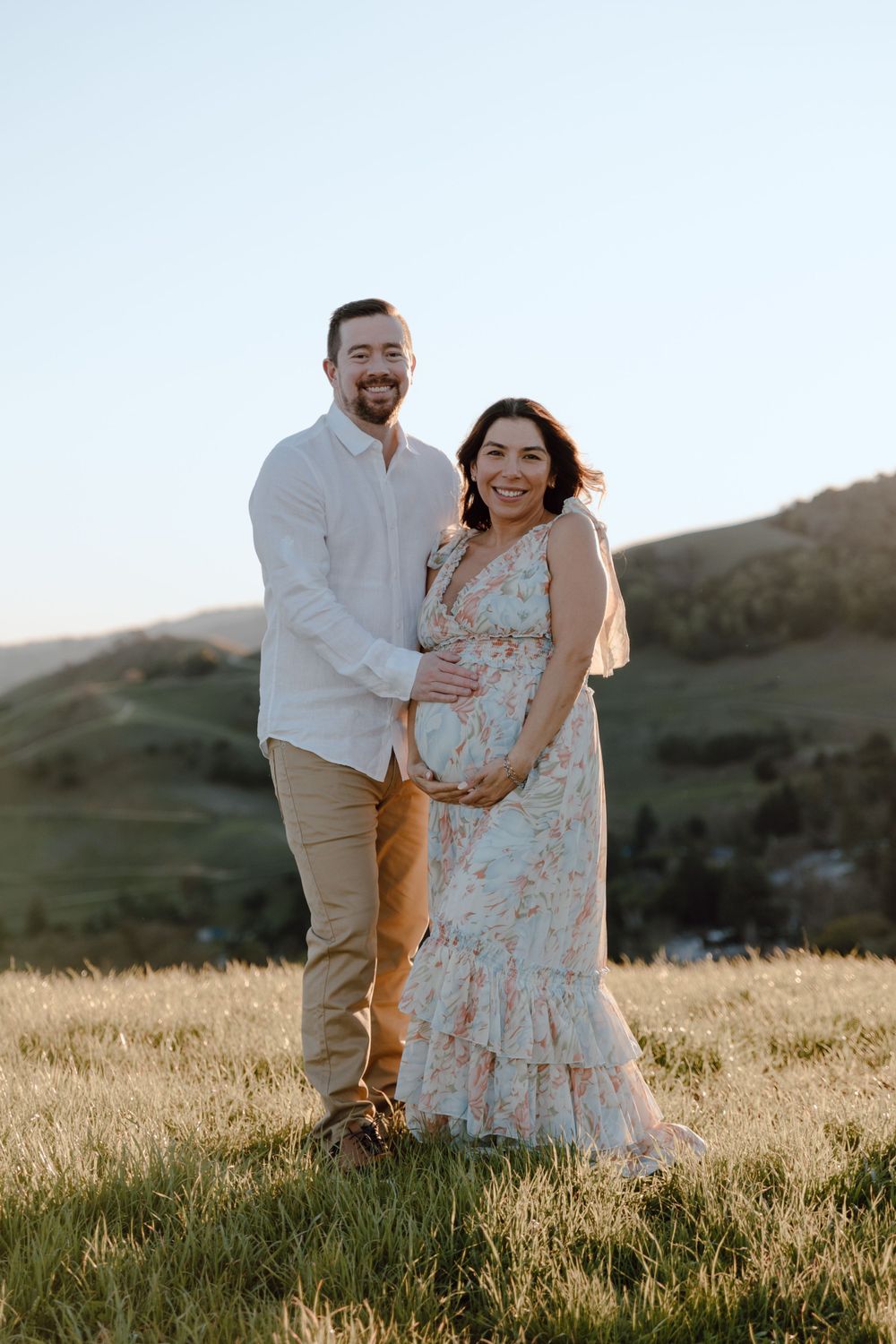 Happy couple posing in grassy field during golden hour maternity photoshoot.