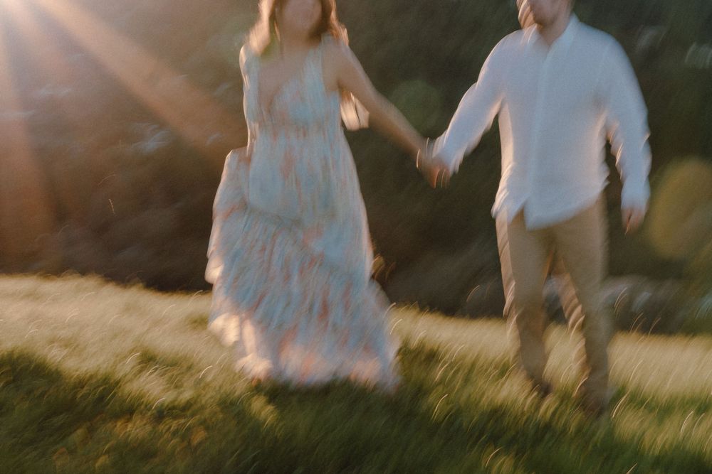 Motion blur capture of couple running through sunlit field in formal attire.