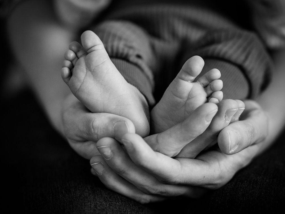 Adult hands gently cradle tiny newborn baby feet in black and white artistic photograph.
