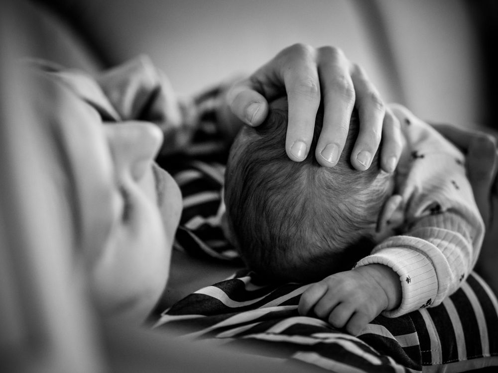 A tender black and white photograph showing a parent's hand gently cradling the head of a sleeping newborn baby.