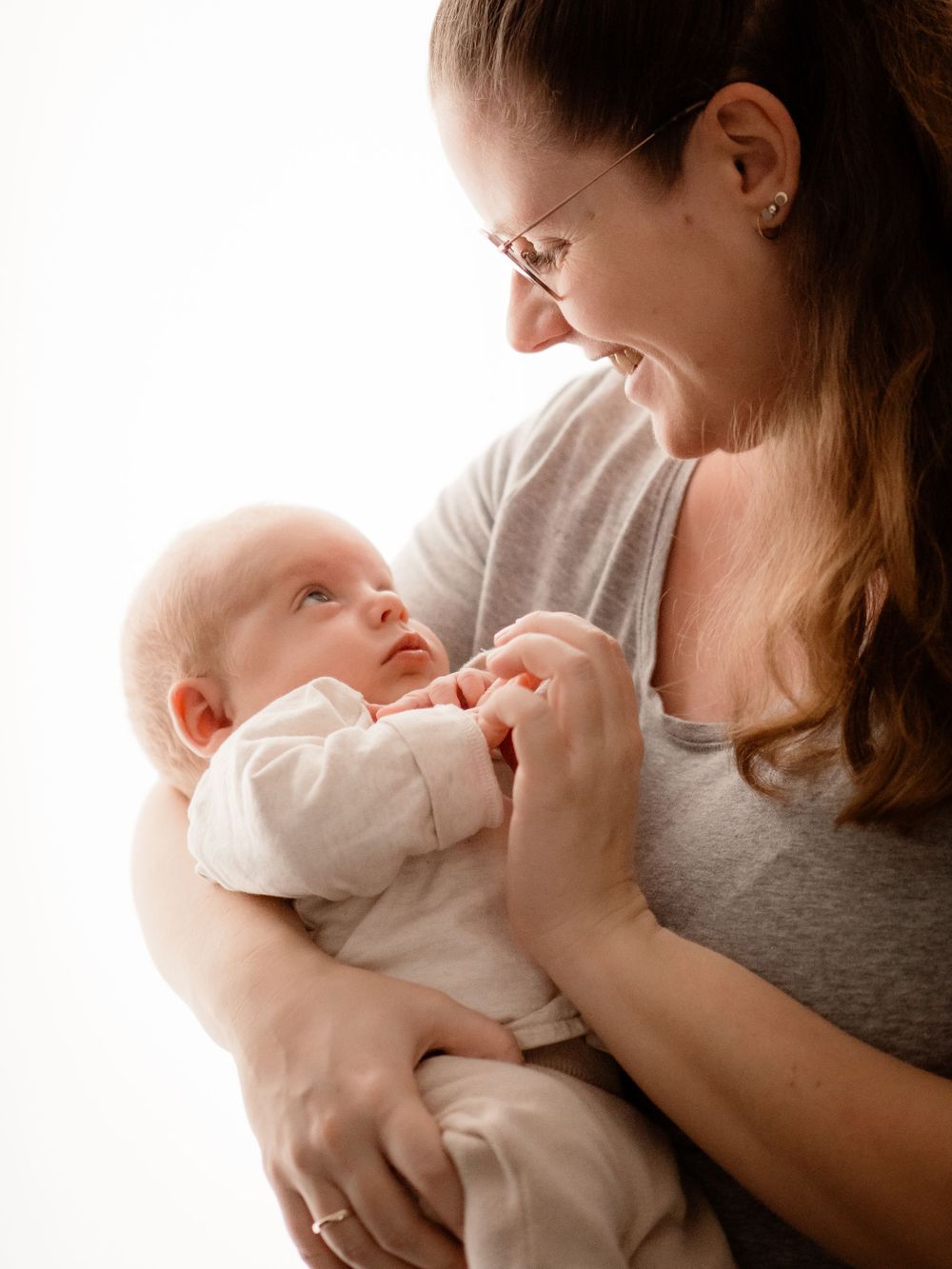 A tender moment shows parent and newborn baby bonding in soft lighting while sharing an intimate gaze.