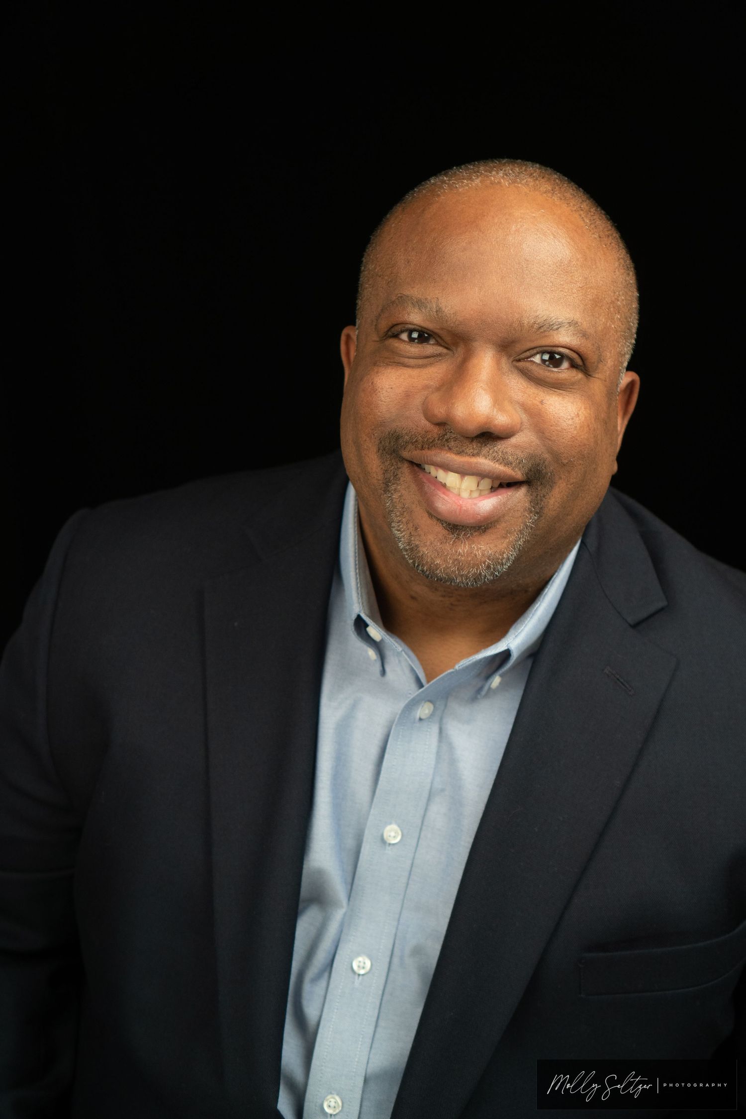 Professional headshot of businessman in suit against black background.