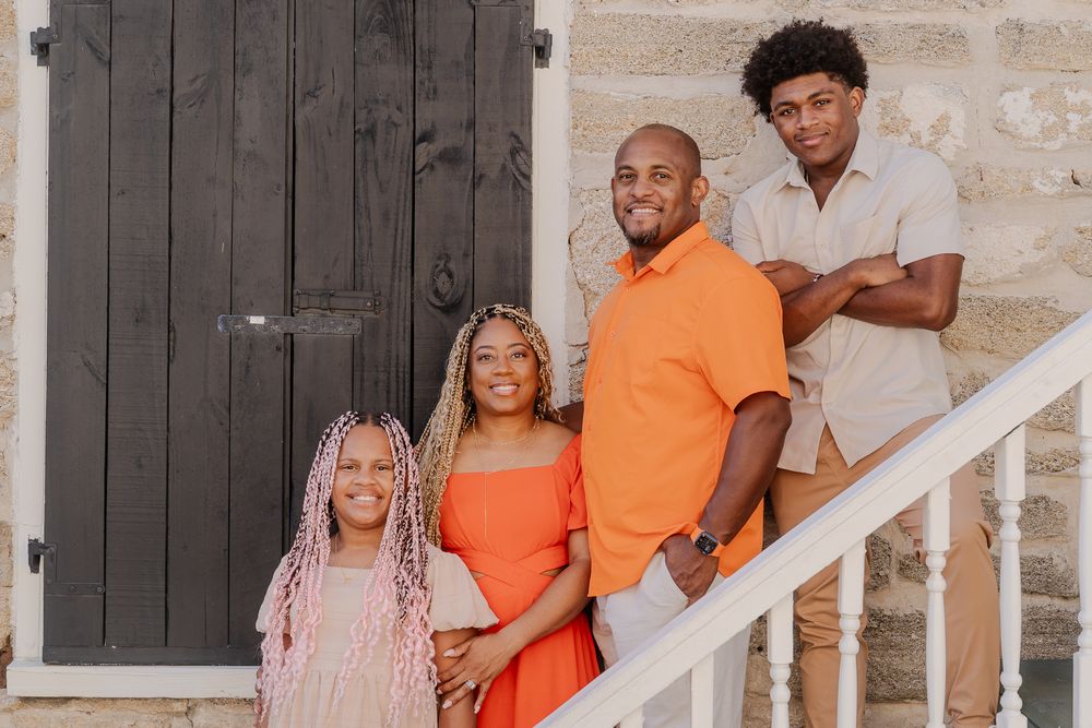 A large family group wearing coordinated orange and white outfits poses together on white stairs.