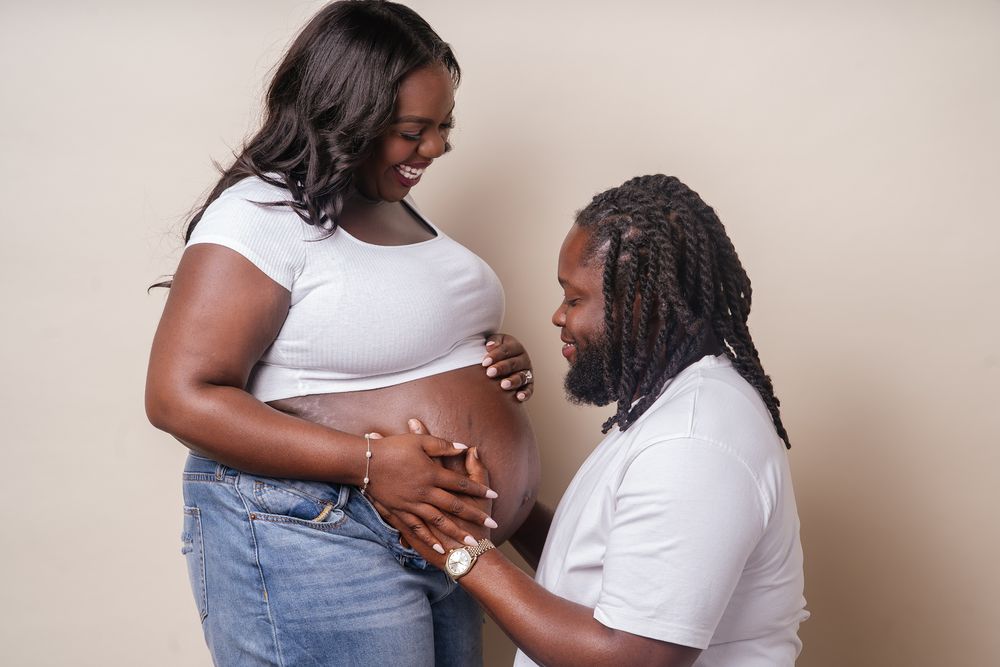People in light colored t-shirts and denim embrace in an intimate photoshoot against a neutral wall.