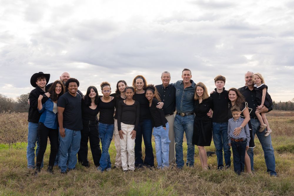 Large extended family poses together for a group photo outdoors against a cloudy sky.