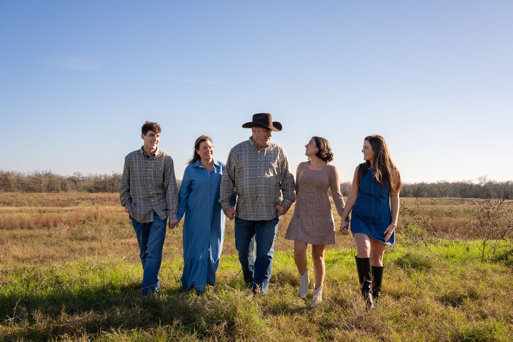 Five people walk together through a sunny field wearing casual clothing on an autumn afternoon.
