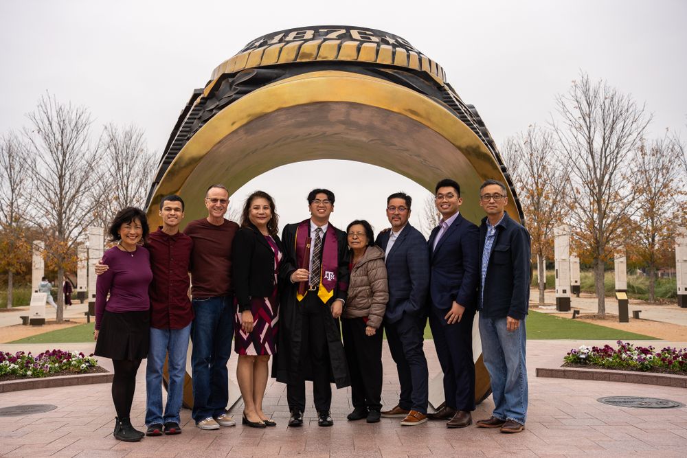 Graduation group photo of students and supporters standing under a golden architectural archway.