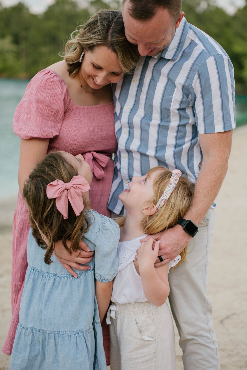 A family in coordinated pastel outfits share a tender moment together on the beach at sunset.