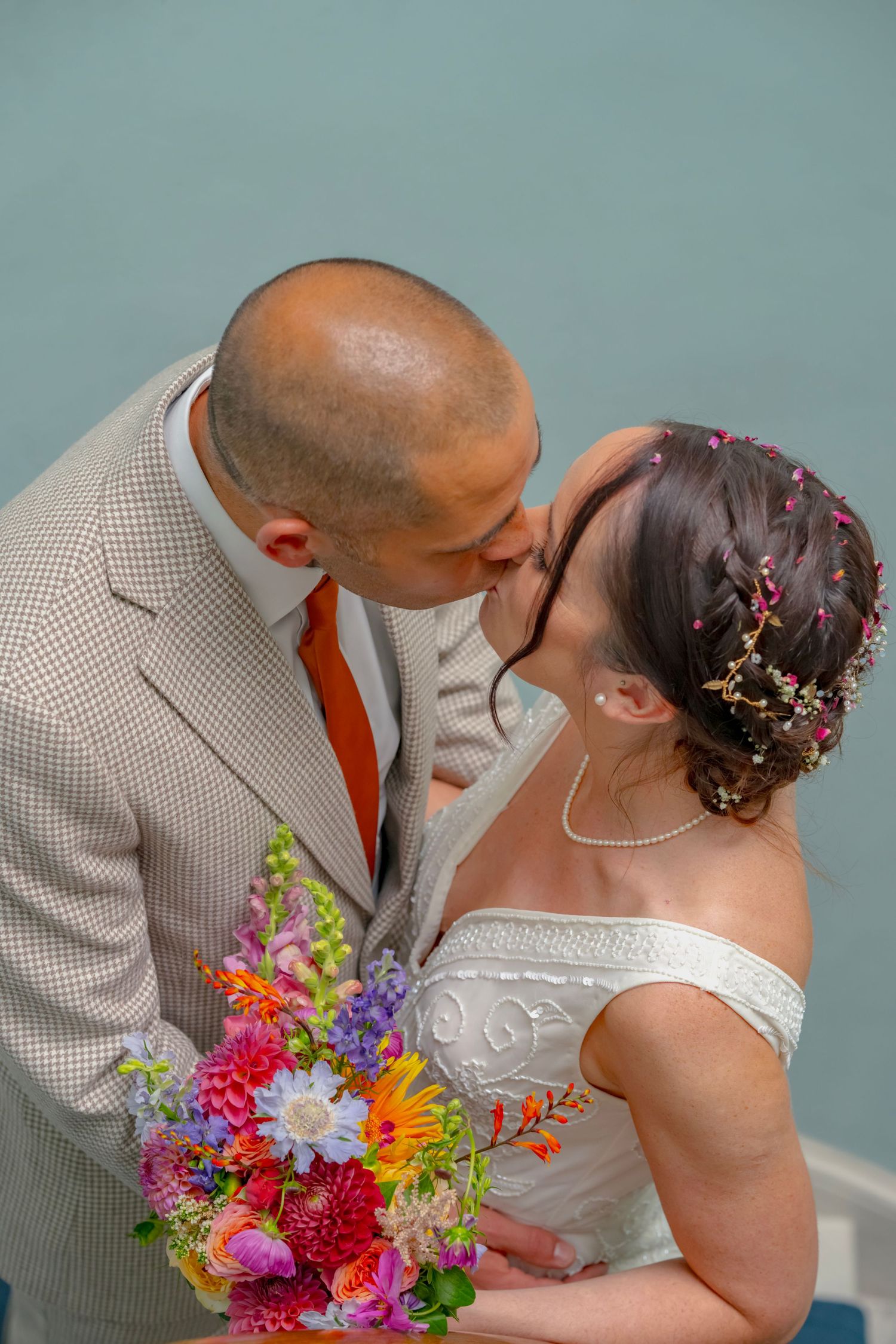 A couple shares a tender kiss while holding a vibrant wildflower bouquet against a blue backdrop.
