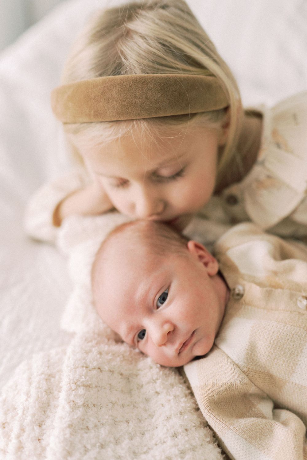 Close-up of siblings sharing an intimate moment on white bedding.