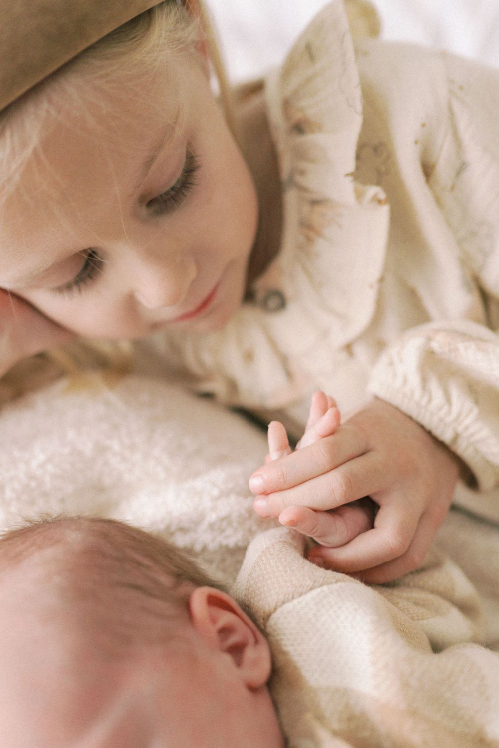 A gentle moment of connection between children on soft white bedding.